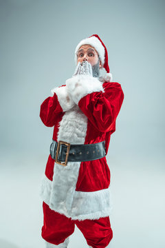 Funny surprised guy with christmas hat posing at studio. New Year Holiday. Christmas, x-mas, winter, gifts concept. Man wearing Santa Claus costume on gray. Copy space. Winter sales.