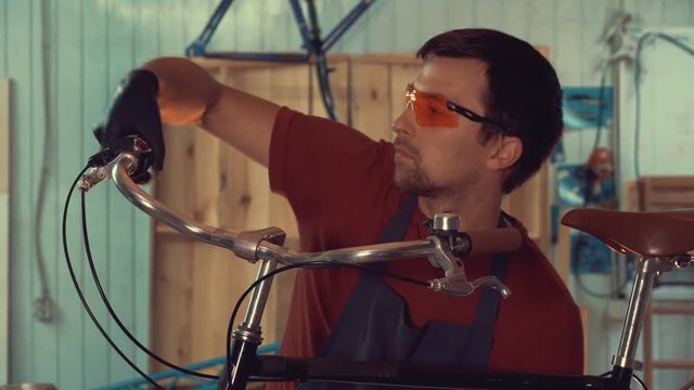 theme small business bike repair. A young Caucasian brunette man wearing safety glasses, gloves and an apron insists the speed switches on the bicycle handlebar in the garage of the workshop