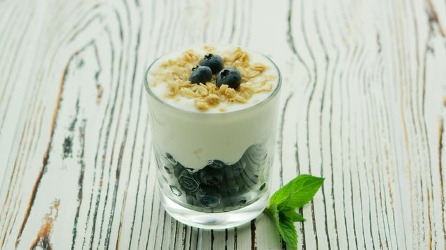 Served snack in glass with layered blueberries and yogurt topped with granola on wooden table