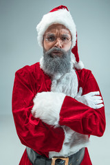 Funny serious guy with christmas hat posing at studio. New Year Holiday. Christmas, x-mas, winter, gifts concept. Man wearing Santa Claus costume on gray. Copy space. Winter sales.