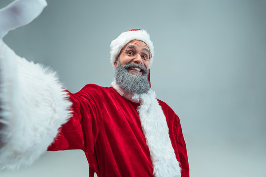 Funny guy with christmas hat posing at studio. New Year Holiday. Christmas, x-mas, winter, gifts concept. Man wearing Santa Claus costume on gray. Copy space. Winter sales.