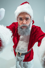 Funny serious guy with christmas hat posing at studio. New Year Holiday. Christmas, x-mas, winter, gifts concept. Man wearing Santa Claus costume on gray. Copy space. Winter sales.