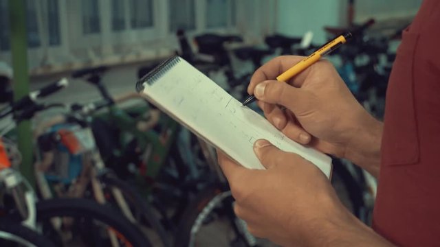 theme of small business selling bicycles. Young Caucasian male brunette small business owner, store manager uses notepad and pen makes notes, checklist at bicycle store