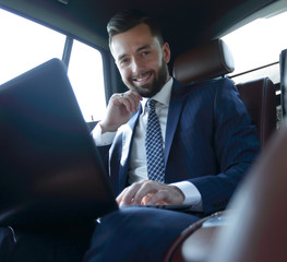 Caucasian male business executive travelling by a car and working on laptop computer.