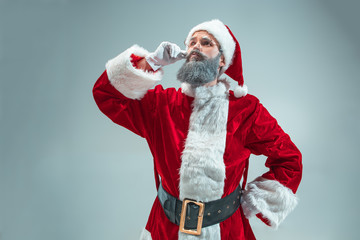 Funny serious guy with christmas hat posing at studio. New Year Holiday. Christmas, x-mas, winter, gifts concept. Man wearing Santa Claus costume on gray. Copy space. Winter sales.