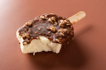 side view chocolate outer ice cream with peanuts on a brown background with some bites