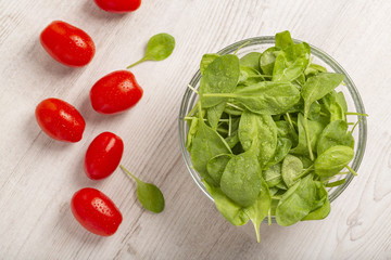 Fresh spinach leaves and tomatoes on light background