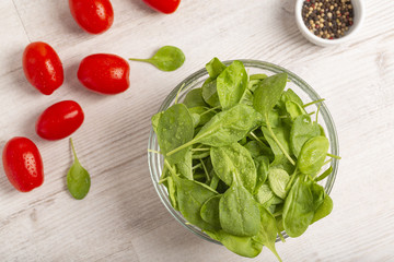 Fresh spinach leaves, tomatoes and other salad ingredients on a light background