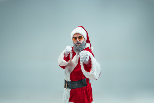 Funny aggressive boxing guy with christmas hat posing at studio. New Year Holiday. Christmas, x-mas, winter, gifts concept. Man wearing Santa Claus costume on gray. Copy space. Winter sales.
