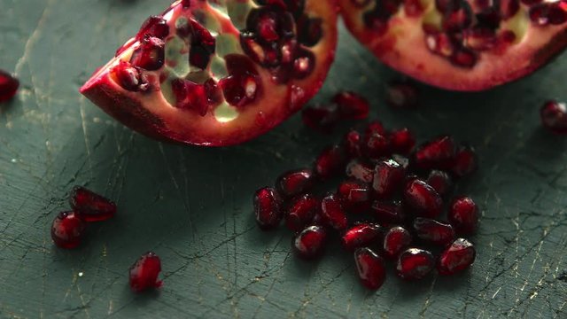 Closeup shot of halves of delicious pomegranate and pile of ruby pomegranate seeds on table