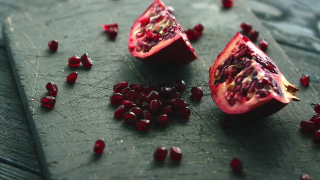 Composed halves of ripe pomegranate with bright shiny ruby-colored seeds on rough board