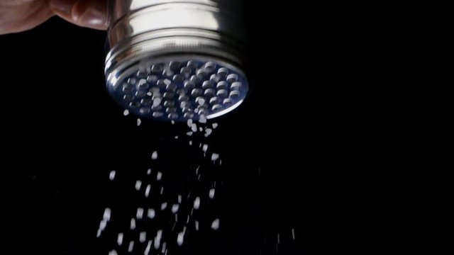 Salt flies straight into the camera on black background. Bottom view. Slow motion.
