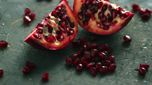 Closeup shot of bright shiny seeds and halves of juicy pomegranate on rough table