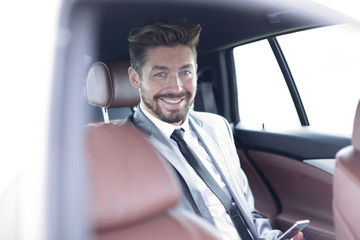 man in suit sitting in car and reading messages on smartphone