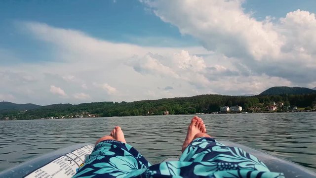 Point of view man relaxing having fun on a floating mattress in Velden Am Worthersee lake mountain view sunny