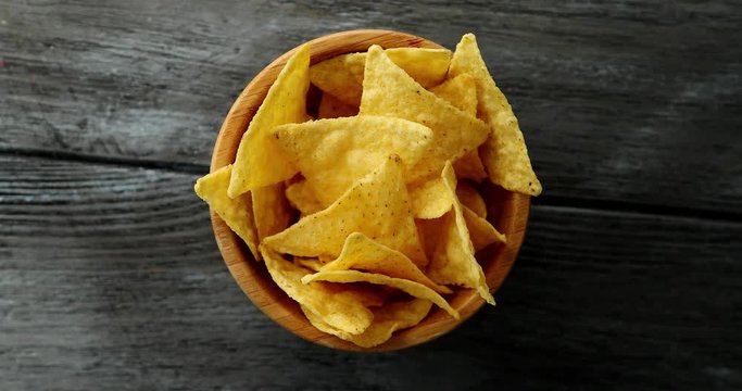 From above shot of round small bowl filled with delicious golden crispy nacho chips and served on gray wooden table