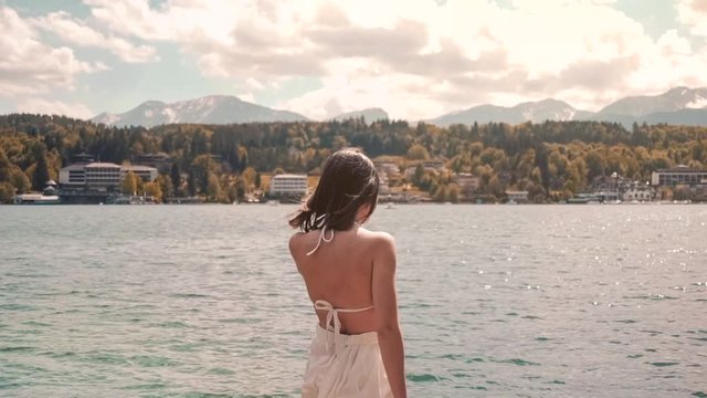 Young woman in swimwear admiring the lake view on a dock in Worthersee lake, Austria mountain view windy hair in slow-motion