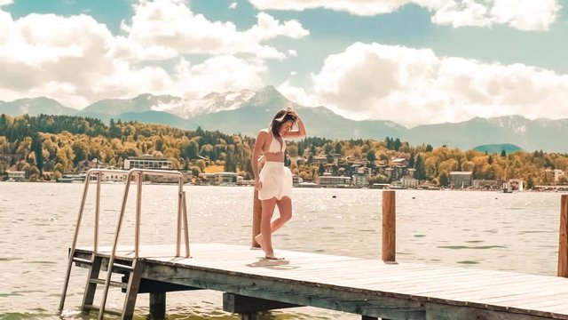 Young woman in swimsuit walking on a dock in Worthersee lake, Austria mountain view windy hair in slow-motion