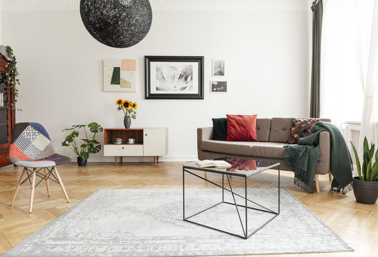 Industrial black coffee table with marble surface and a colorful patchwork chair in a living room interior with mixed style of decor.