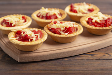 Mini pizza with salami, tomato and cheese on wooden background. Tasty appetizer, tartlet.