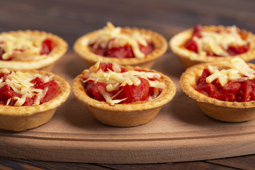 Mini pizza with salami, tomato and cheese on wooden background. Tasty appetizer, tartlet.