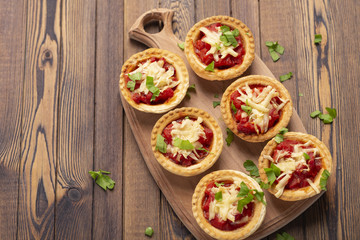Obraz na płótnie Canvas Mini pizza with salami, tomato and cheese on wooden background. Tasty appetizer, tartlet.
