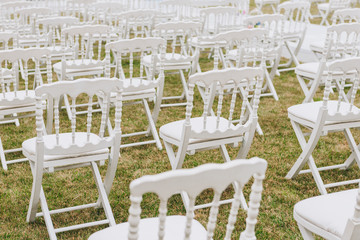 Concept of preparation and waiting for guests as elegant white chairs are set up on a lawn for wedding ceremony