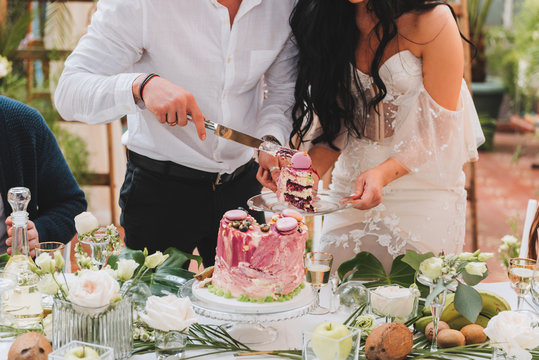Gorgeous bride and groom cutting a small modern wedding cake on a table with various decorations