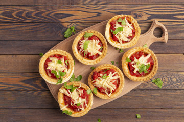 Mini pizza with salami, tomato and cheese on wooden background. Tasty appetizer, tartlet.