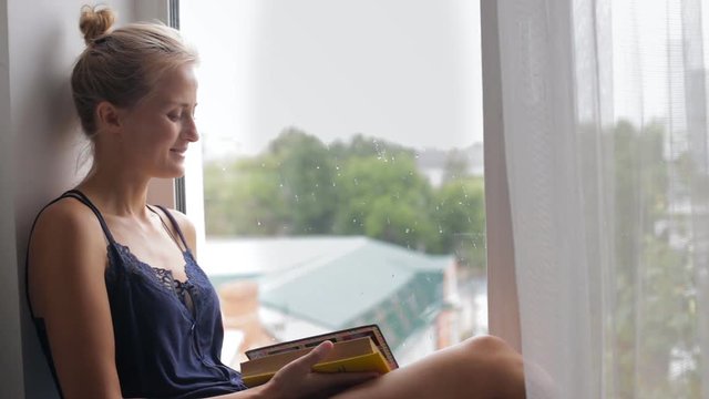 Woman reading, sitting on a window sill