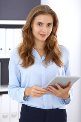 Young brunette business woman looks like a student girl at work in office. Girl standing straight with tablet pc