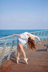 Naklejka premium Young attractive ballerina training on sea coast wearing casual. Fine art ballet concept. Surreal dancing. Slim girl dance on the ocean beach. Active and healthy women