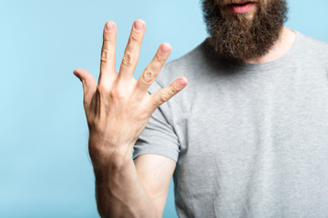 bearded man showing number five with his hand. cropped shot of a male torso on blue background....