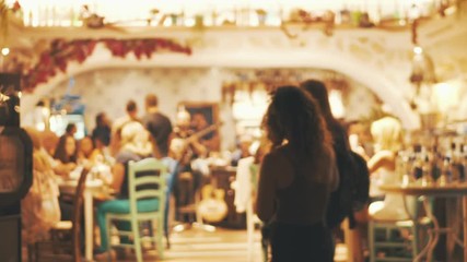 Blurred image of the interior of a large beautiful restaurant with bright lighting, entrance. Tables with chairs await visitors for dinner. Visitors choose their own table. Satisfied customers