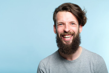 emotion expression. very happy joyful thrilled to bits man with beaming smile. young handsome bearded guy portrait on blue background.