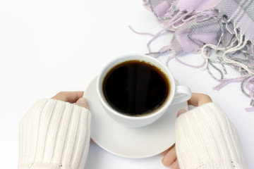 Hands in white sweater holding white ceramic cup of coffee and pink knitted plaid lying near on white, copy space