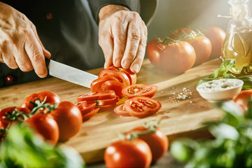Cook chopping bright red tomatoes on cutting board