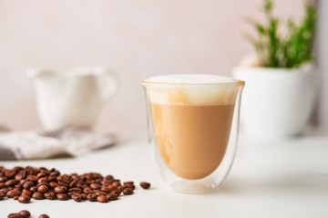 Cappuccino in a double walled glass with roasted coffee beans. Feminine rose background with copy space. High resolution image, narrow depth of field.