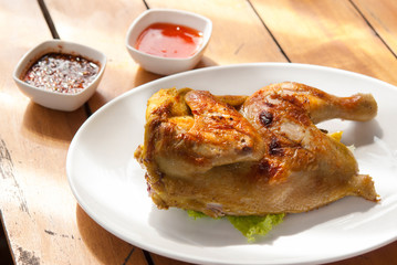 Grilled half chicken whole marinated in fresh yellow turmeric ,honey and soy sauce on a plate with spicy sauce on a wooden table background