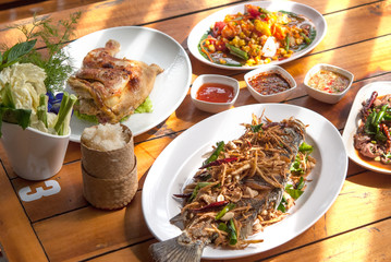 Delicious eating Thai food together warm sunlight. Fried whole fish topped Thai herb vegetables in white dish on wooden table background