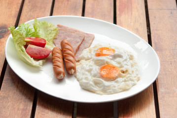 Morning breakfast, Fried egg, sausage and ham in white dish on wooden table together warm light in the morning