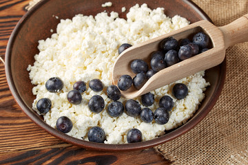 Cottage cheese with ripe blueberries in a clay bowl with a wooden spoon.