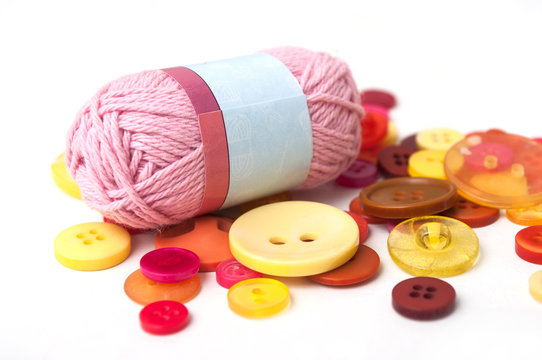 closeup of red and orange buttons and pink wool ball on white background