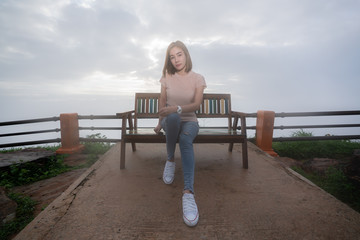 Beautiful asian woman in casual sitting on bench behind a beautiful sunset pass through sky clouds