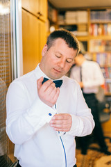 Portrait of a stunning groom dressing up for the wedding and getting ready in his room. Groomsmen...