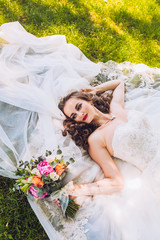 Wedding day of newlyweds. The bride lying on the grass. Beautiful bride with long veil and fashion...