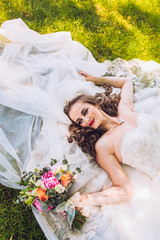 Wedding day of newlyweds. The bride lying on the grass. Beautiful bride with long veil and fashion...