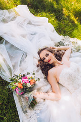 Wedding day of newlyweds. The bride lying on the grass. Beautiful bride with long veil and fashion...