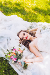 Wedding day of newlyweds. The bride lying on the grass. Beautiful bride with long veil and fashion...