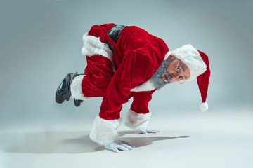 Funny serious guy with christmas hat dancing at studio. New Year Holiday. Christmas, x-mas, winter, gifts concept. Man wearing Santa Claus costume on gray. Copy space. Winter sales.